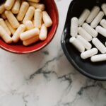 Top view of red and black ceramic bowls filled with assorted capsules on marble surface.